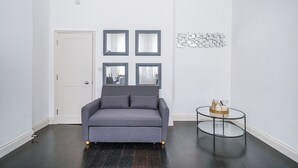 Ein Zimmer mit einer grauen Couch, einem kleinen runden Tisch und einer weißen Tür.