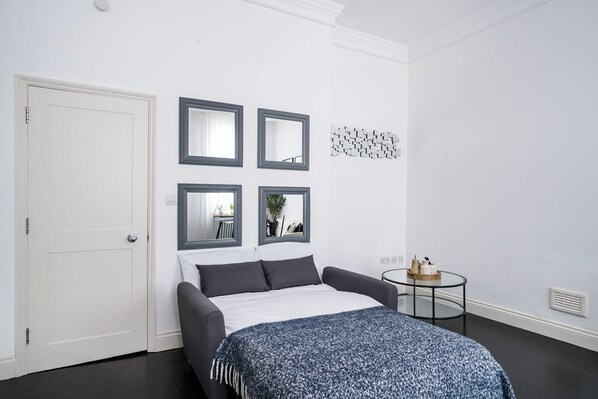 A bedroom with a bed, a white door, and a small round table with decorative items. - Hans Road Flat (London)