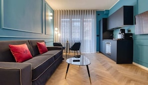 A modern living room with a sofa, a small round table, and a kitchen area with a stove and cabinets. - Suite House of Mirrors - Luxury Apartment in Buenos AIres Gallery (Milano)