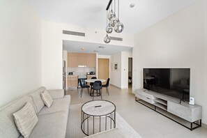 A modern living room with a sofa, a round coffee table, a TV, and a dining area with chairs and a table. - 1BR Balcony & Luxury Amenities (Dubai)