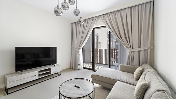 Ein modernes Wohnzimmer mit einem Flachbildfernseher, einem runden Couchtisch, einem beigefarbenen Sofa und einem Balkon mit Vorhängen.
