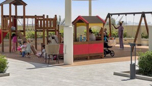Ein Spielplatz mit Schaukeln, einem Spielhäuschen und einem schattigen Bereich.
