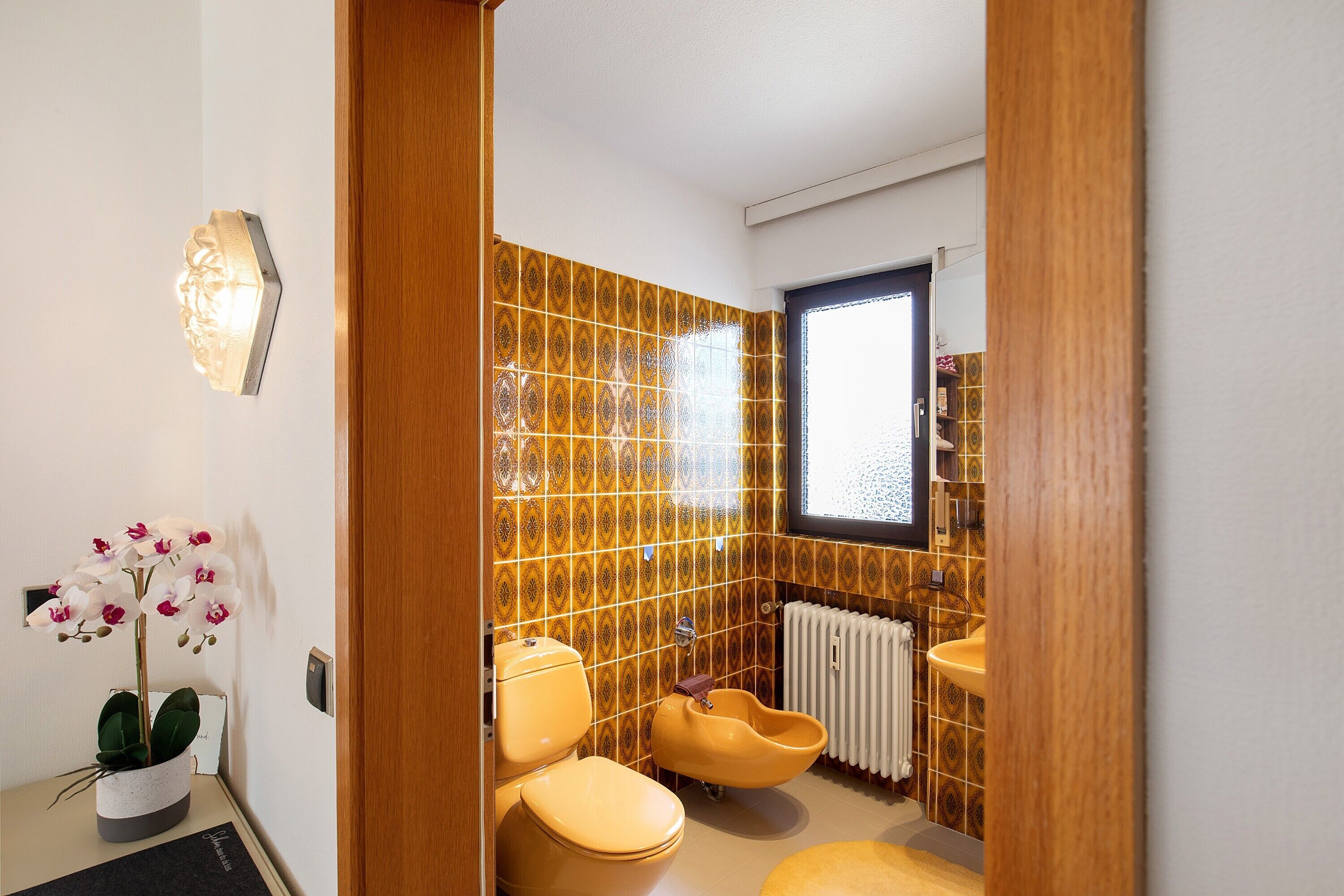 Ein Badezimmer mit Toilette, Bidet und Waschbecken, mit gemusterten Fliesen und einer Orchidee im Topf.