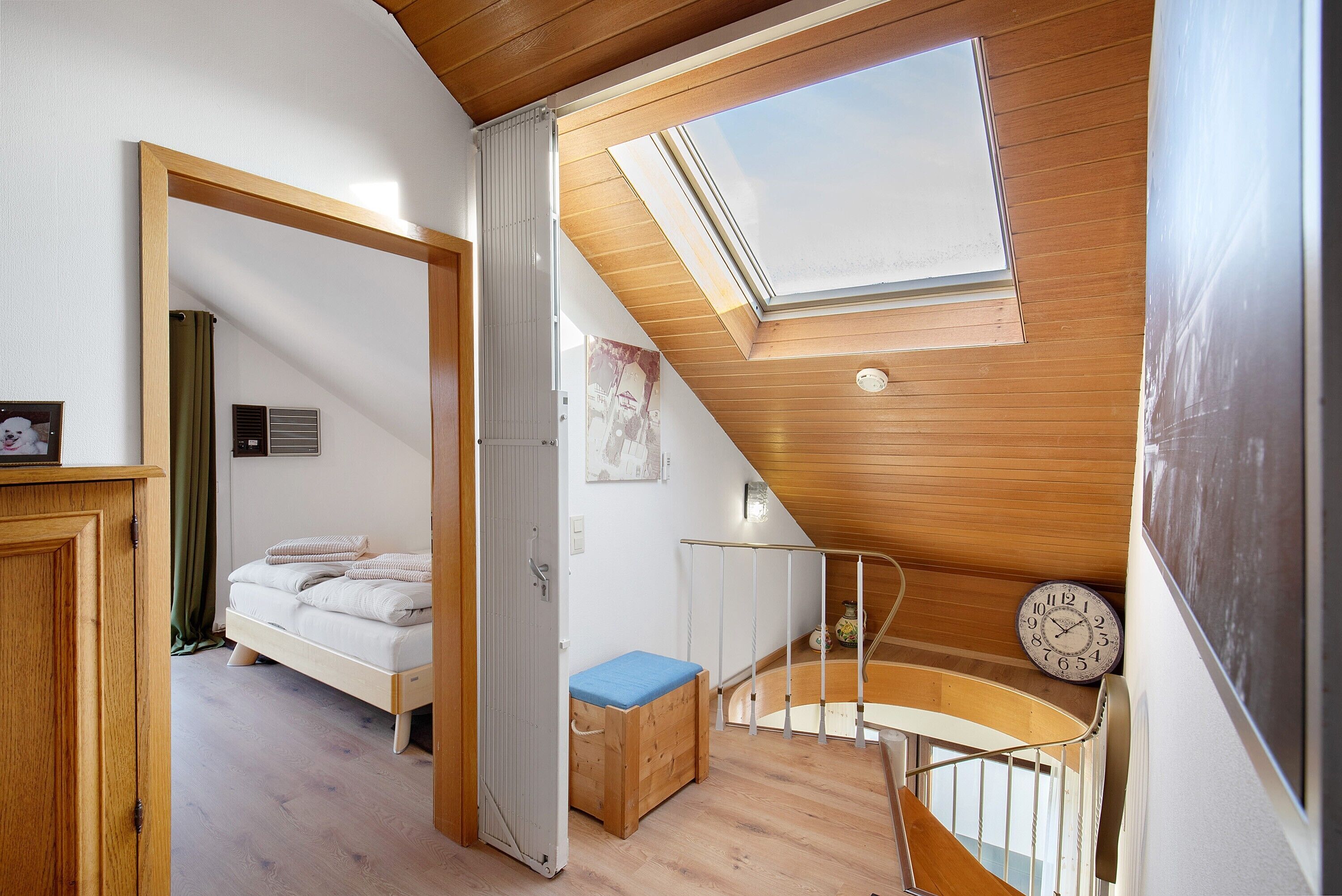 A bedroom with a skylight, a bed, a wooden bench, and a staircase.