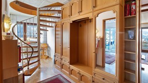 A wooden staircase with a spiral design leading to an upper floor, a large wooden wardrobe with multiple doors, and a bookshelf with books and decorative items. - Apartment "Omas volle Hütte" with Mountain View, Private Terrace and Wi-Fi (Mühltal)