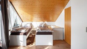 A bedroom with a sloped ceiling, a bed, a small table, and a window with curtains. - Apartment "Omas volle Hütte" with Mountain View, Private Terrace and Wi-Fi (Mühltal)