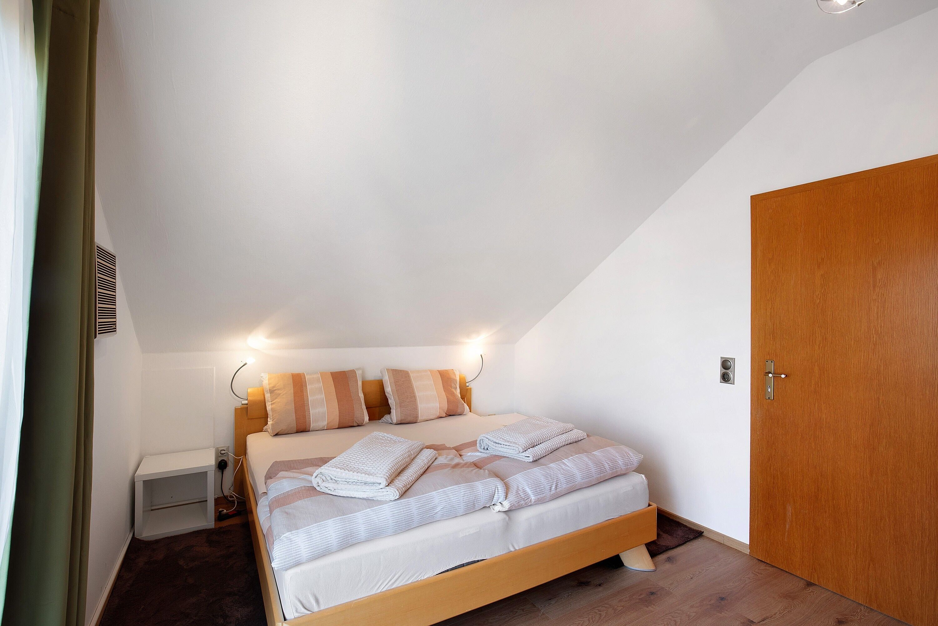 A bedroom with a bed, bedside tables, a wooden door, and a ceiling light.
