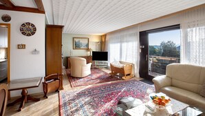 A living room with a sofa, a dining table, a TV, and a balcony with a view. - Apartment "Omas volle Hütte" with Mountain View, Private Terrace and Wi-Fi (Mühltal)