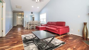 Un salon spacieux avec un canapé d’angle rouge, une table basse noire et un tapis à motifs.