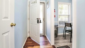 Un couloir avec une porte blanche, une fenêtre avec des stores et une chaise.