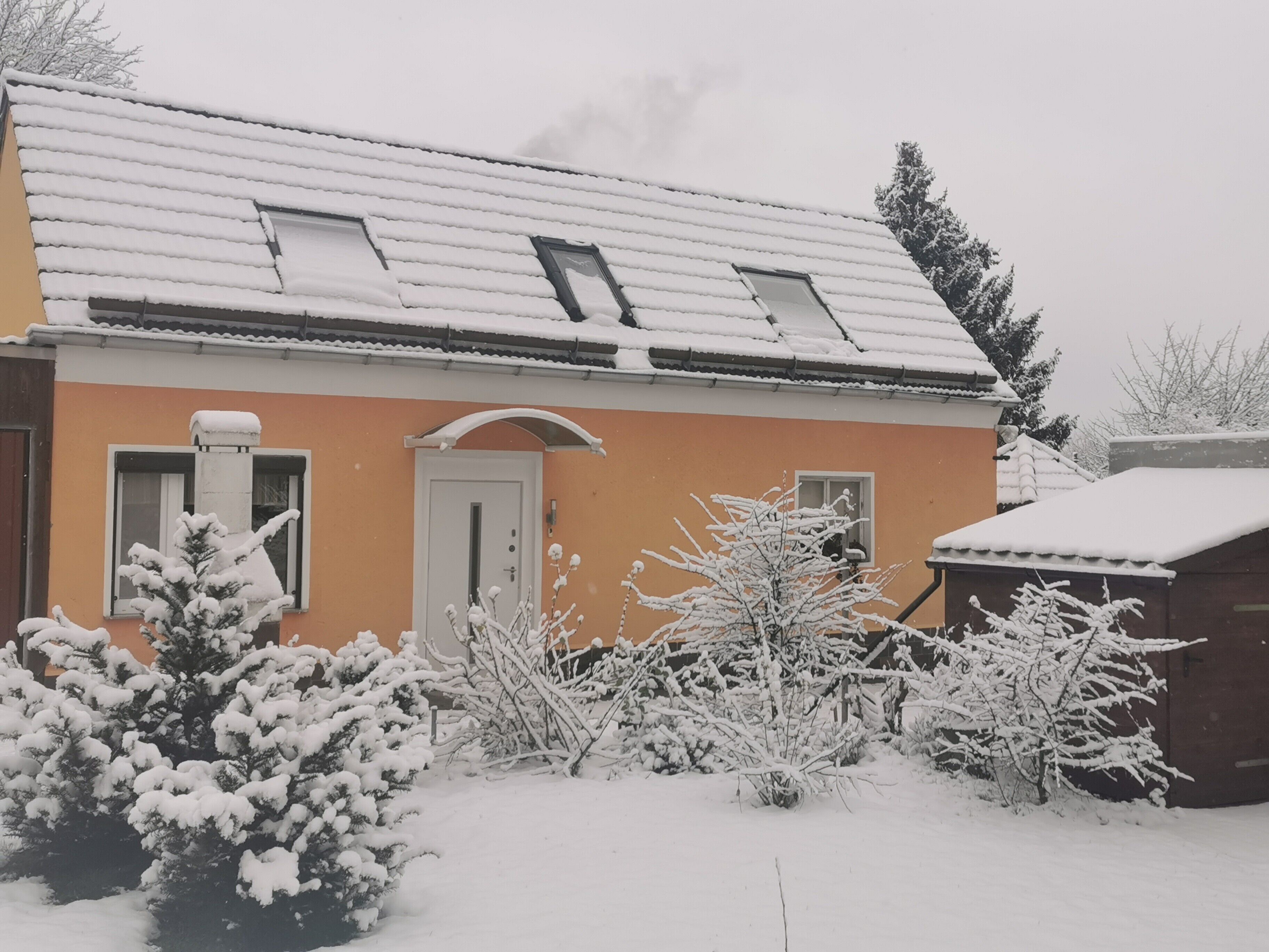 Ein Haus mit schneebedecktem Dach, einer sichtbaren Tür und Fenstern.