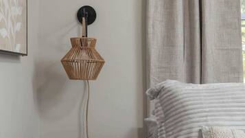 Une chambre à coucher avec un lit, une table de chevet, une lampe fixée au mur et une fenêtre avec des rideaux.