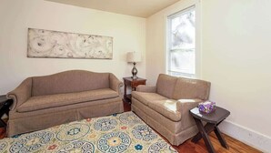 Una sala de estar con dos sofás beige, un tapete estampado, una mesita con lámpara y una ventana con persianas.