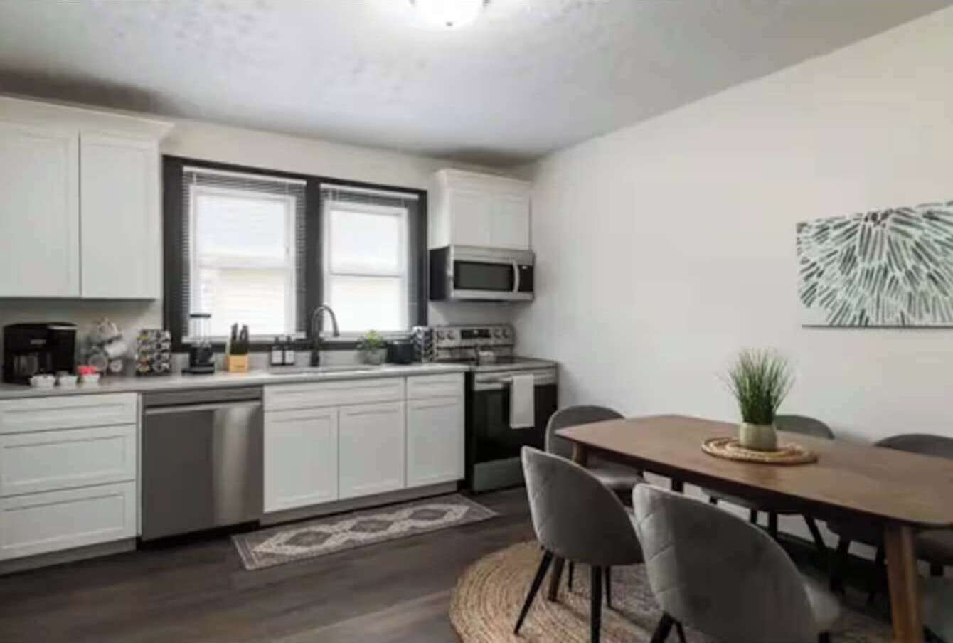 A modern kitchen with white cabinets, a microwave, and a dining area with a wooden table and chairs.
