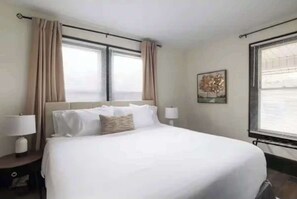 A hotel room with a large bed, two bedside tables with lamps, and a window with blinds. - Modern 3BR Executive Suite – Steps from Old Salem & Downtown (Winston-Salem)
