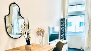 A hotel room with a wooden desk, two black chairs, a mirror, a vase with flowers, a flat-screen TV, and a window with curtains. - Luxury 7 Bedroom Apartment Sleeps 16 (Vienna)