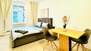 A compact room with a bed, a dining table with chairs, a window with curtains, and a potted plant. - Luxury 7 Bedroom Apartment Sleeps 16 (Vienna)
