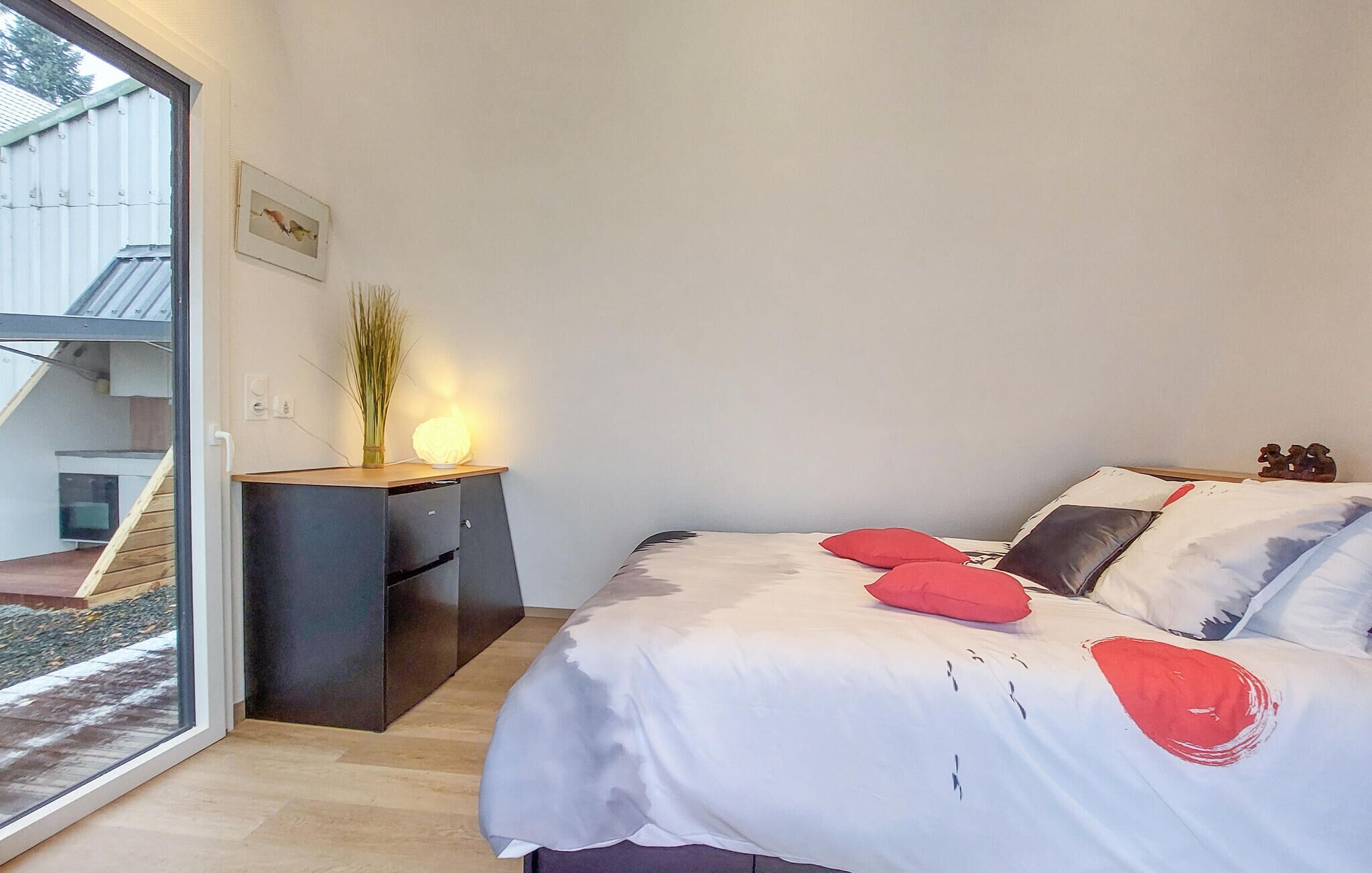 A bedroom with a bed, a nightstand, a lamp, and a window.