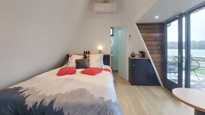 A bedroom with a bed, pillows, a bedside table, a lamp, a wardrobe, and a view of a lake through large windows. - Awesome home in Herry with heated swimming pool (Herry)