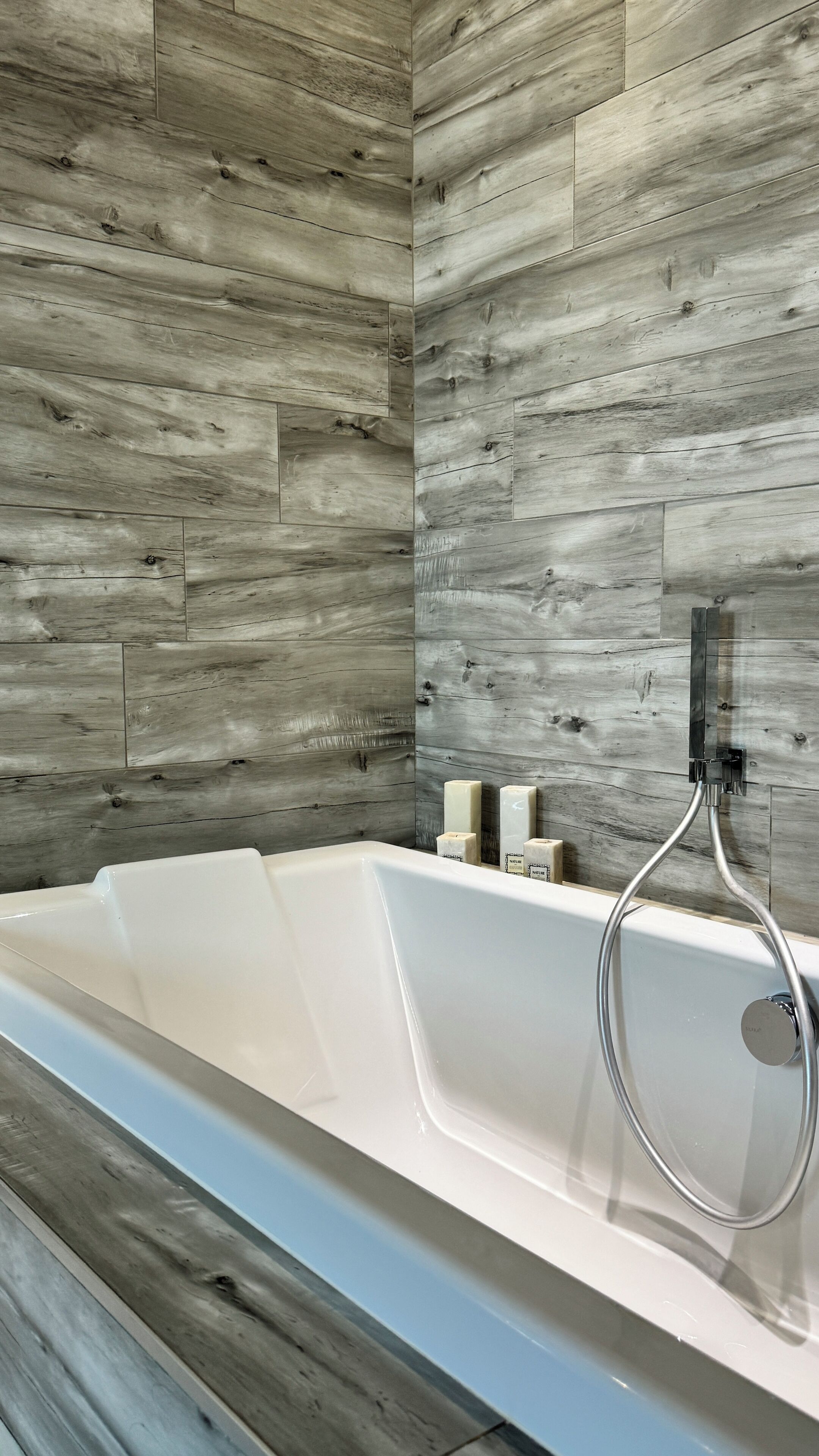Une salle de bain moderne avec un mur revêtu de panneaux en bois, une baignoire blanche et une douchette à main.
