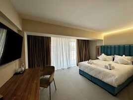 Habitación de hotel con cama, escritorio, silla, televisor y cortinas.