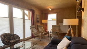 Ein Holzinnenraum mit einer Couch, zwei Sesseln, einem Glastisch und einer Lampe.