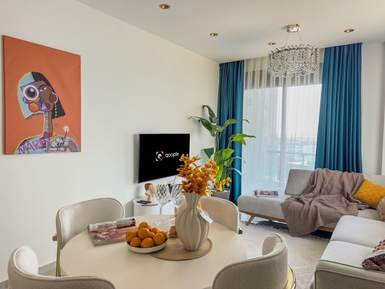 A modern living room with a dining area, a TV, and a large window with blue curtains.
