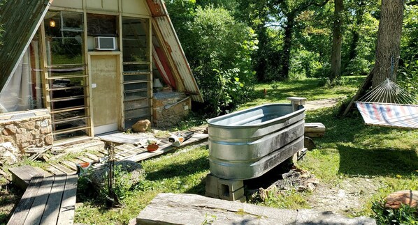 Una cabaña rústica con fachada de piedra, terraza de madera y un depósito de agua metálico.