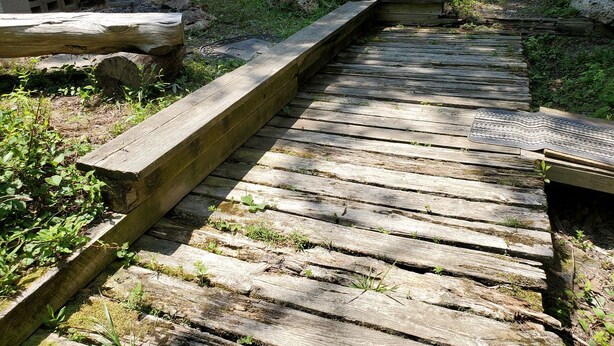 Un paseo marítimo de madera que atraviesa un área natural con rocas y follaje.