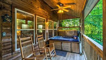 A wooden cabin with a deck, a hot tub, and two rocking chairs.