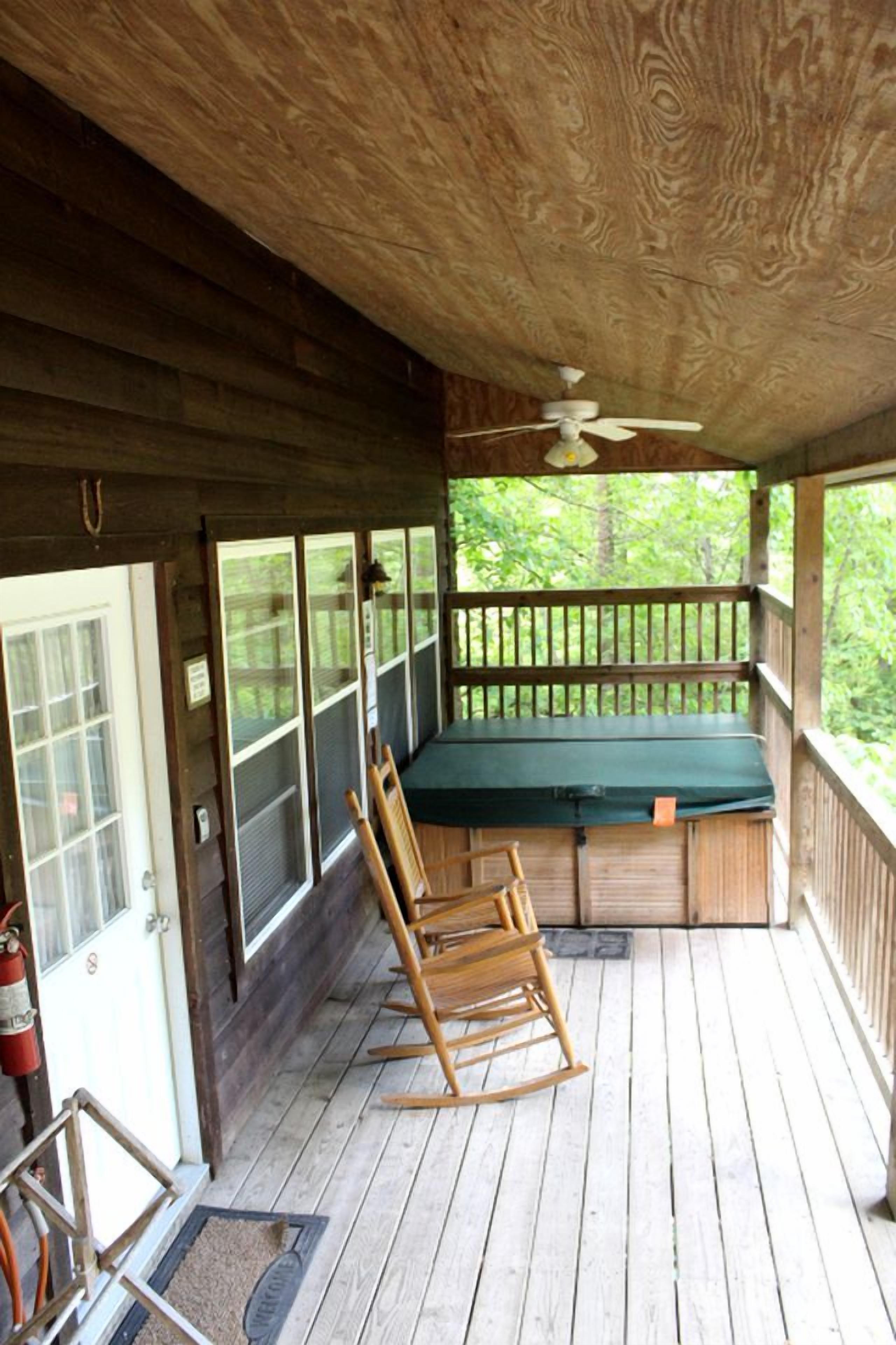 A covered porch with a ceiling fan, a rocking chair, a bench, and a view of the outdoors.