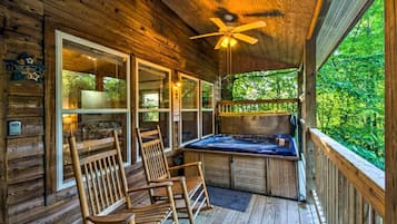 A wooden cabin with a deck, a hot tub, and two rocking chairs.