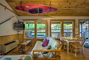 A cabin interior with a bed, a table, chairs, a heater, and large windows. - Tree-House Style Cabin with Forest Views, Nantahala National Fores, North Carolina (Bryson City)