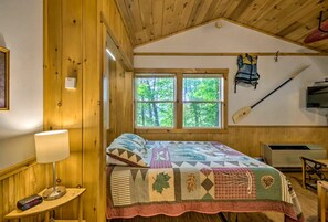 Ein Schlafzimmer einer Holzhütte mit einem Bett, einem Fenster, einer an der Wand befestigten Kajak und einem Heizgerät.