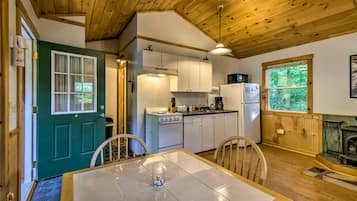 A compact kitchen with a stove, refrigerator, and cabinets, a dining table with chairs, and a window with a view of greenery.