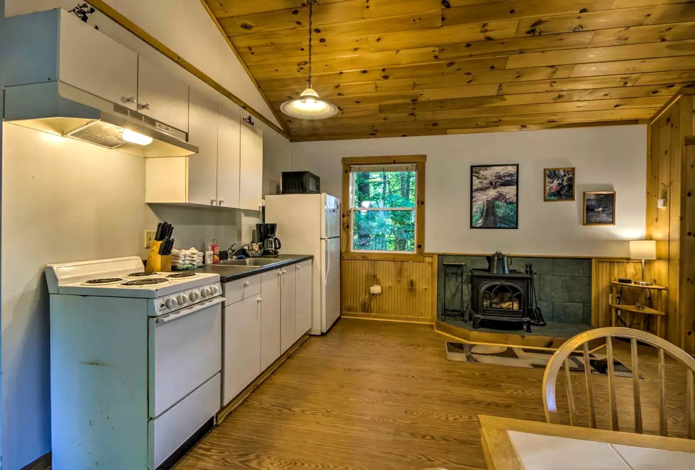 A kitchen with a stove, sink, and refrigerator, a dining area with a table and chairs, and a wood-burning stove.