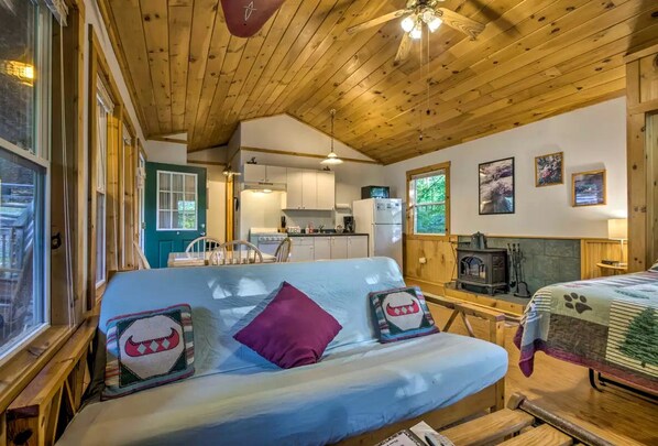 Un intérieur de chalet chaleureux avec un plafond en bois, un coin cuisine, un canapé agrémenté de coussins décoratifs et une cheminée.