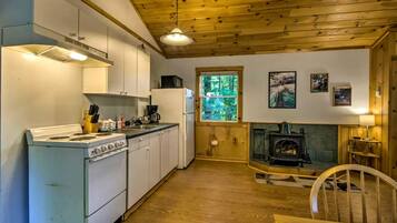 A kitchen with a stove, sink, and refrigerator, a dining area with a table and chairs, and a wood-burning stove.