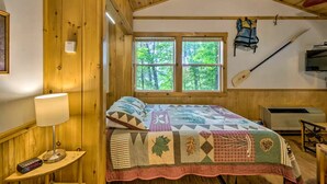 A wooden cabin bedroom with a bed, a window, a wall-mounted kayak, and a heater. - Tree-House Style Cabin with Forest Views, Nantahala National Fores, North Carolina (Bryson City)
