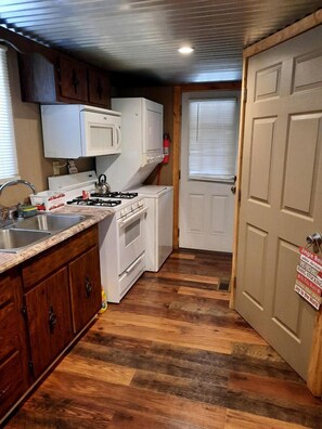 A compact kitchen with white appliances, wooden cabinets, and a wooden floor.