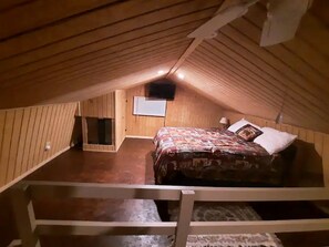 A small attic bedroom with wooden walls, a single bed, and a sloped ceiling.
