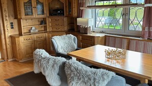 A cozy kitchen with wooden cabinets, a dining table with chairs, and a window with curtains. - Cozy holiday home with mountain views (Breitenbach am Inn)