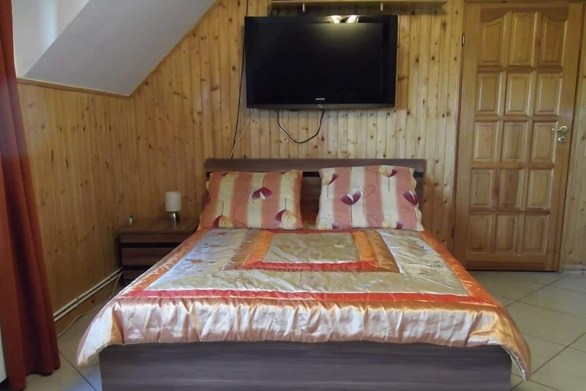 A bedroom with a bed, wooden walls, a television mounted above the bed, and a wooden door.