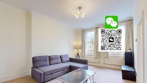 A modern living room with a grey sofa, a glass coffee table, a lamp, and a window with curtains. - Philbeach Gardens Flat (London)