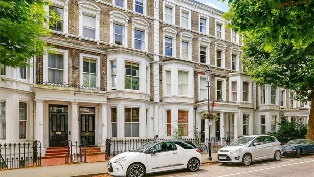 A row of three-story townhouses with white facades and brick detailing. Each townhouse has a black front door and a small front garden. - Philbeach Gardens Flat (London)