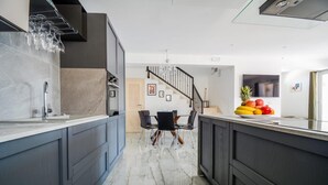 Una cocina moderna con armarios oscuros, encimera de mármol y comedor con candelabro.