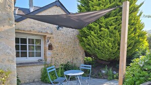 Een stenen huis met een raam, een terras met een tafel en stoelen, en een barbecue.