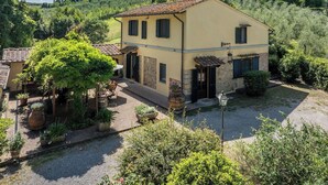 A two-story house with a yellow facade, a tiled roof, and a small garden area with potted plants and a pathway. - Podere La Botte, Pool, Lari (Lari)