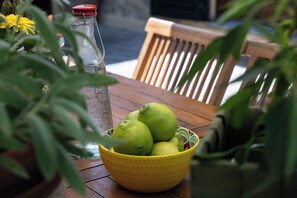 Ein Holztisch mit einer gelben Schüssel voller grüner Früchte, einer Glasflasche und einer Blumentopf-Pflanze.