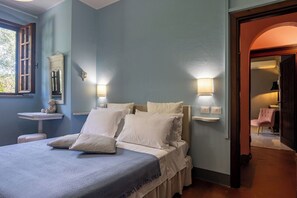 Une chambre à coucher avec un lit, des lampes de chevet, une table de chevet, une fenêtre et une porte en arc de cercle.